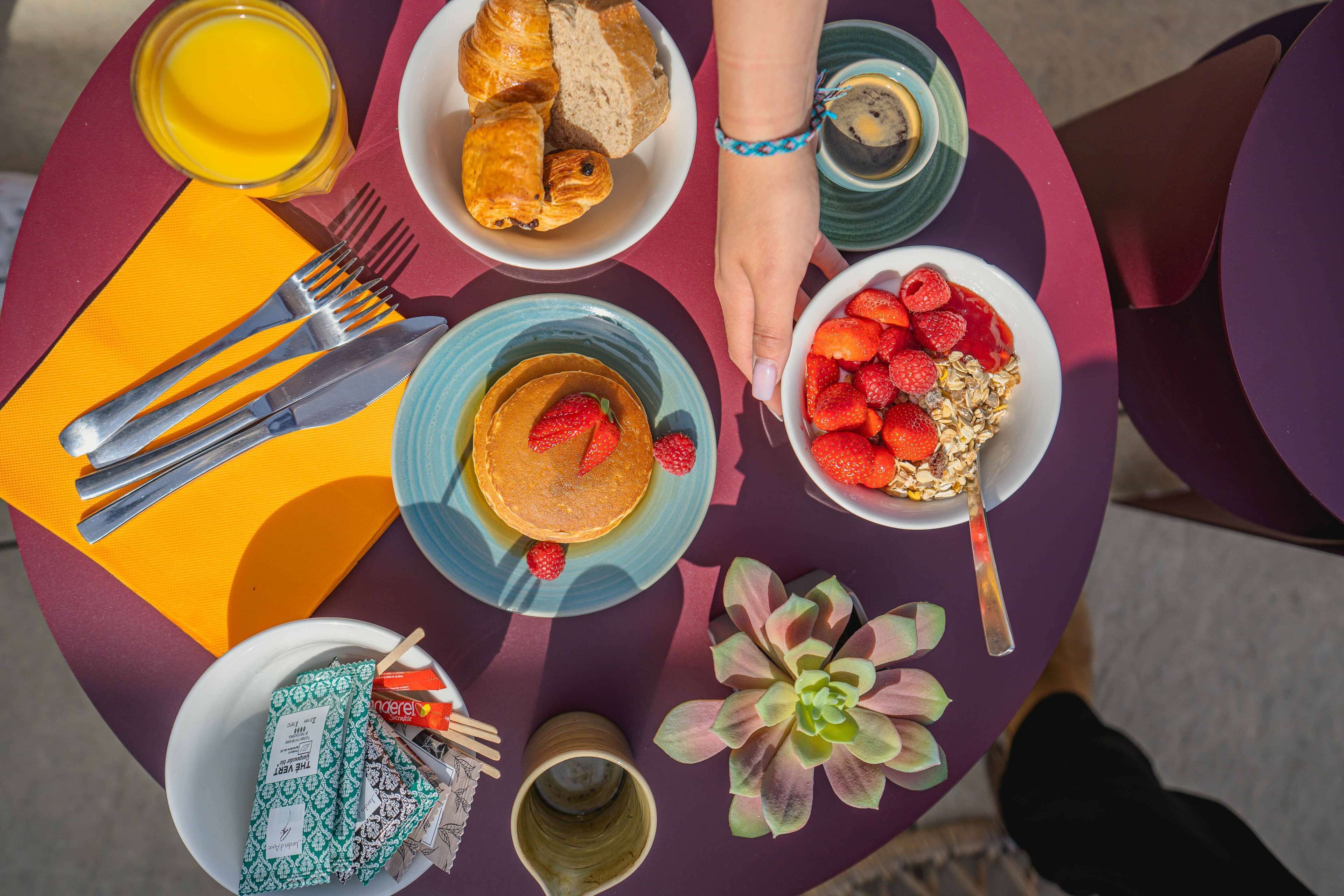 Une table de petit-déjeuner avec des croissants, des crêpes, des fraises et une plante verte.
