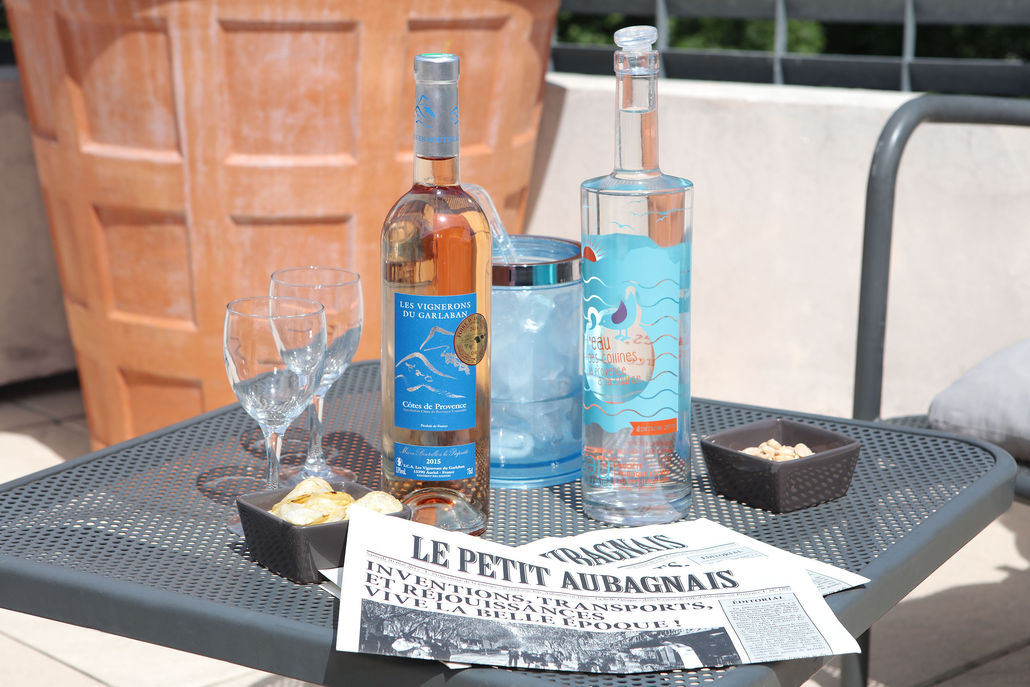 Une table avec des bouteilles, des verres, un bol de noix et un journal.