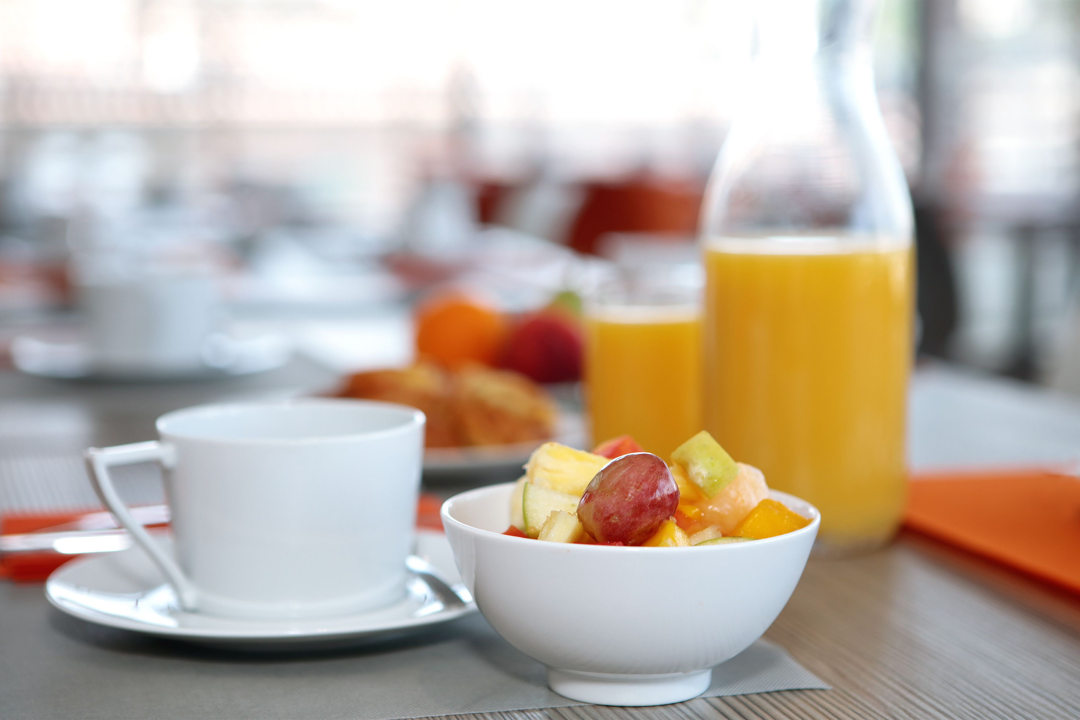 A breakfast setting with a white cup, a bowl of fruit, and a glass of orange juice on a table.