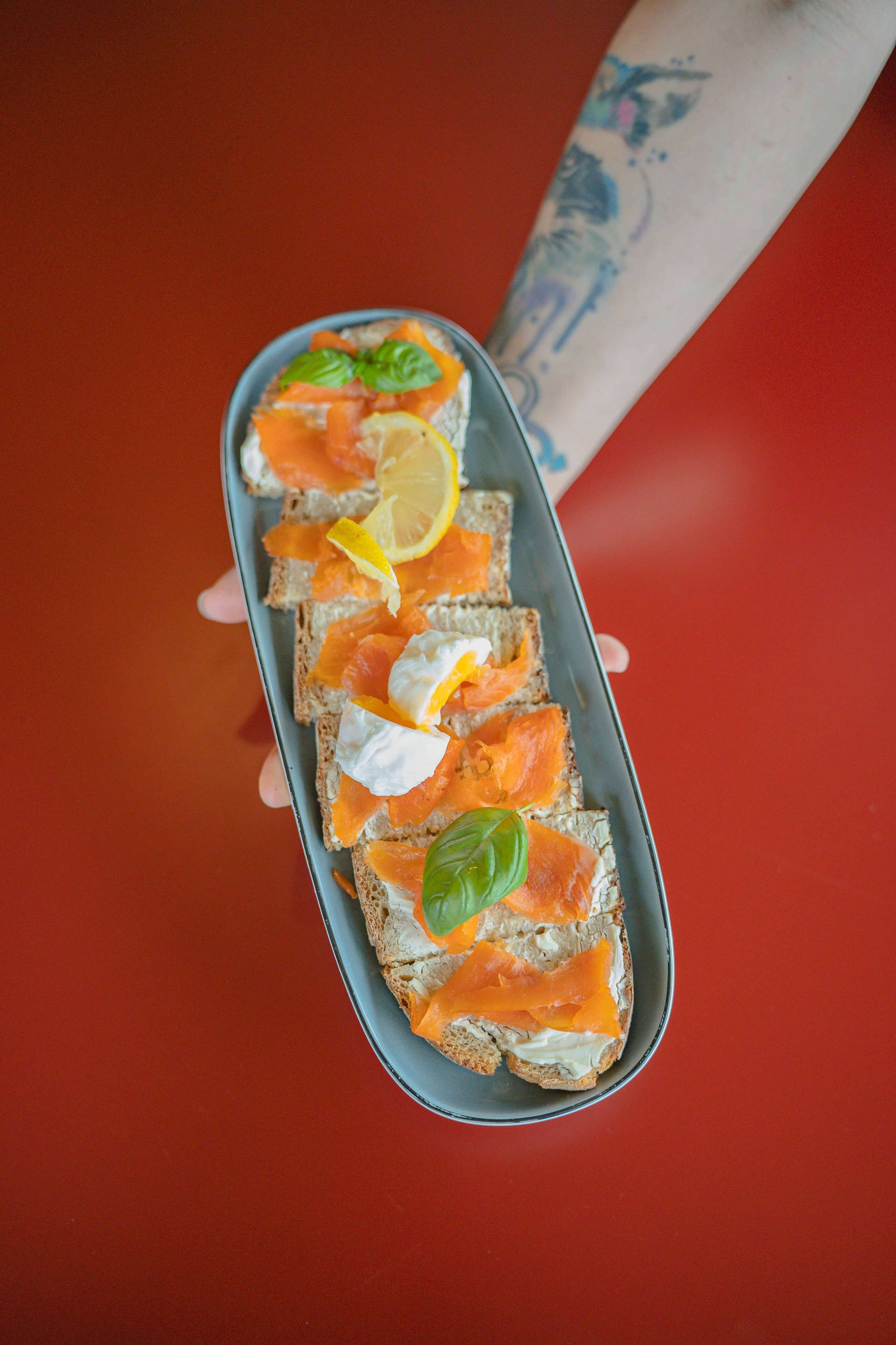 Une assiette de saumon fumé et de fromage frais, servie sur du pain de seigle, et garnie de citron et de basilic.