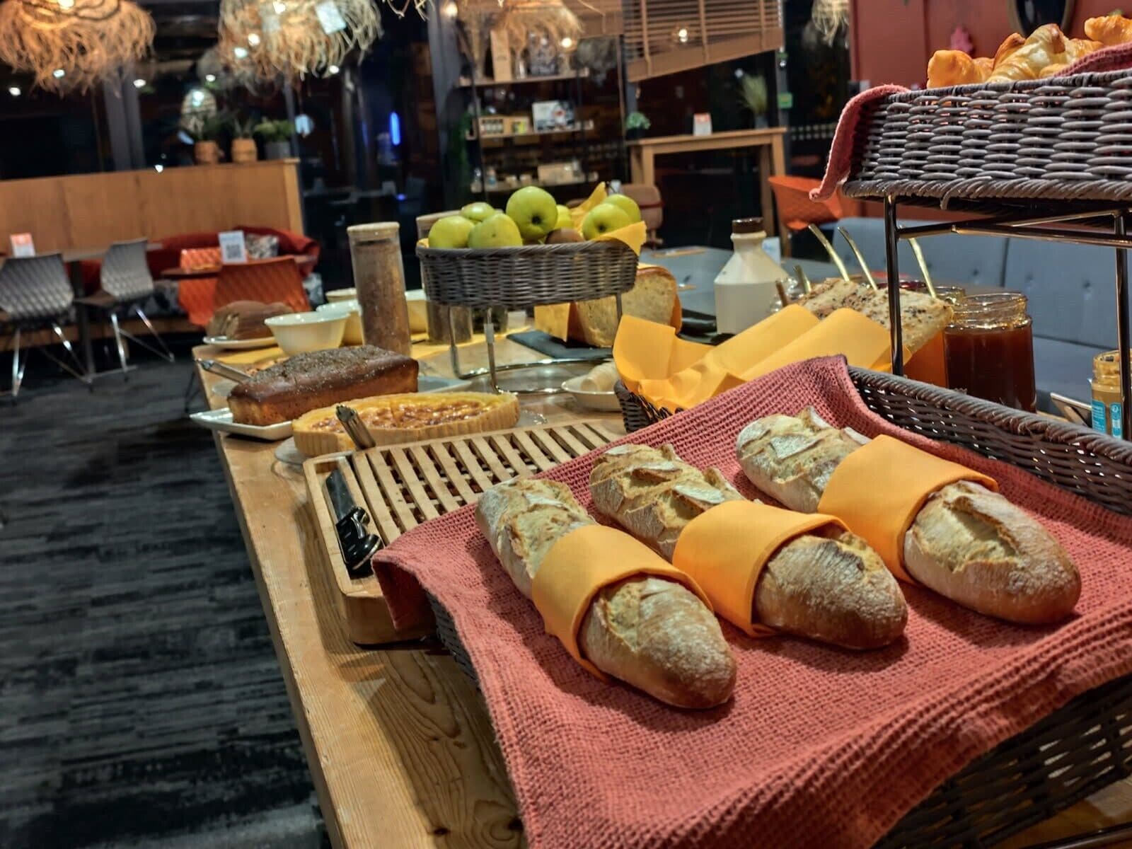 Una mesa de buffet con pan, pasteles y una cesta de frutas.