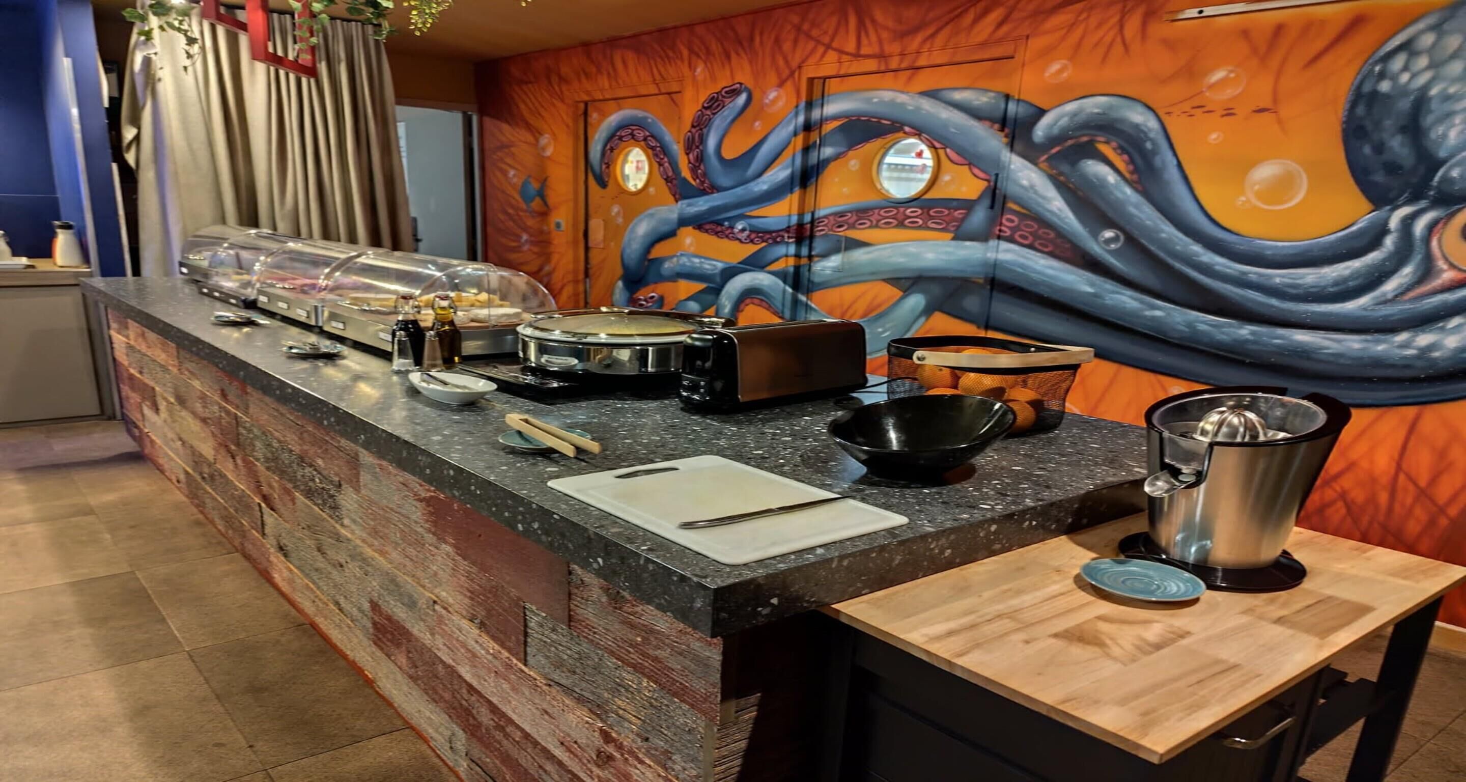 A kitchen counter with a variety of cooking utensils, a juicer, and a decorative octopus mural on the wall.