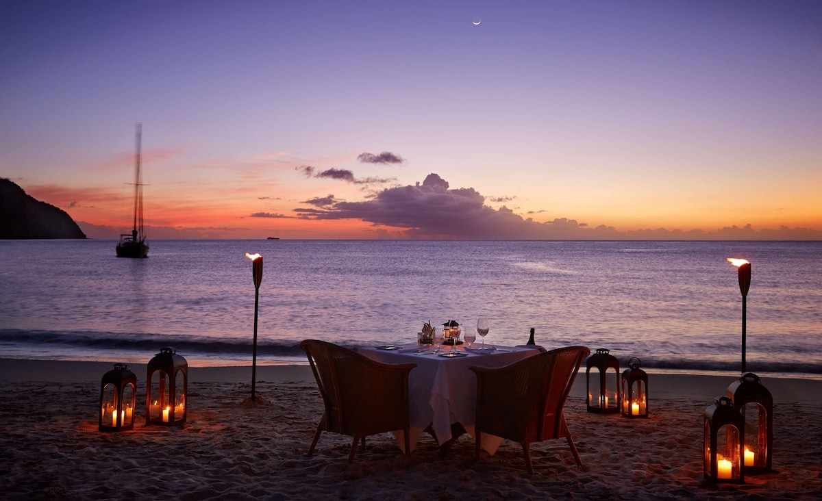 A beachside dining setup with a table and chairs, surrounded by lanterns, overlooking the sea. - Sugar Beach, A Viceroy Resort (Soufrière)
