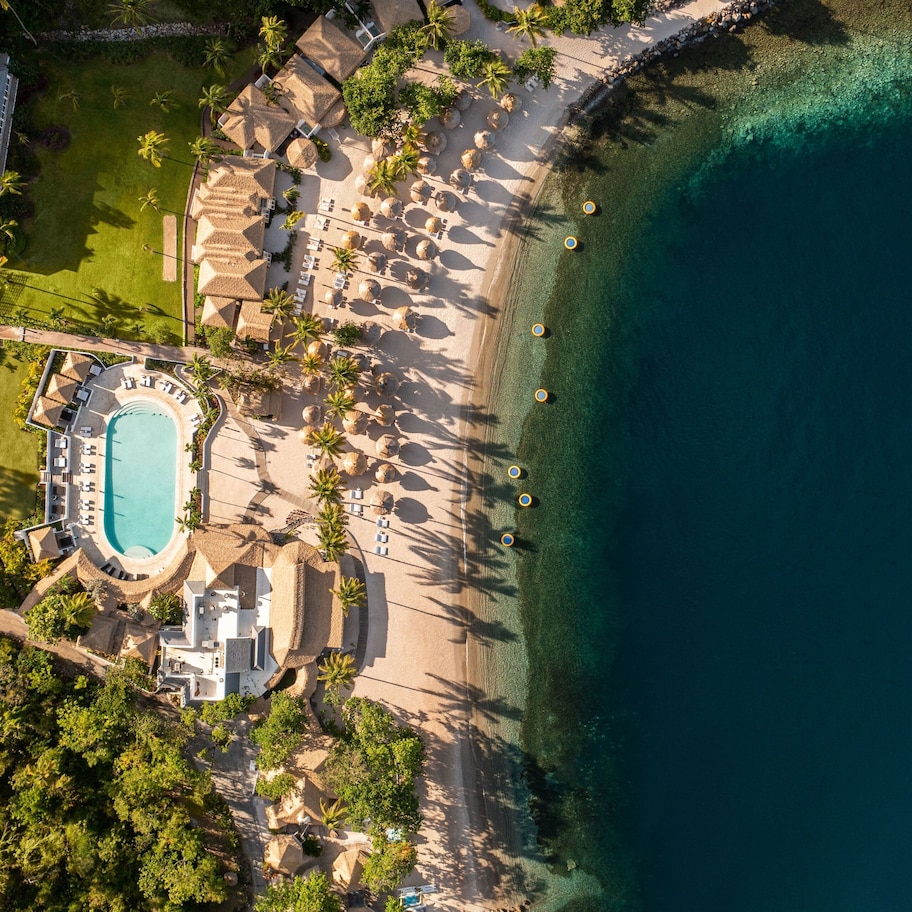 An aerial view of a resort with a swimming pool, beach area, and palm trees.