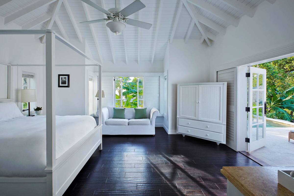 A spacious bedroom with a large bed, a white sofa, a wardrobe, and a ceiling fan.