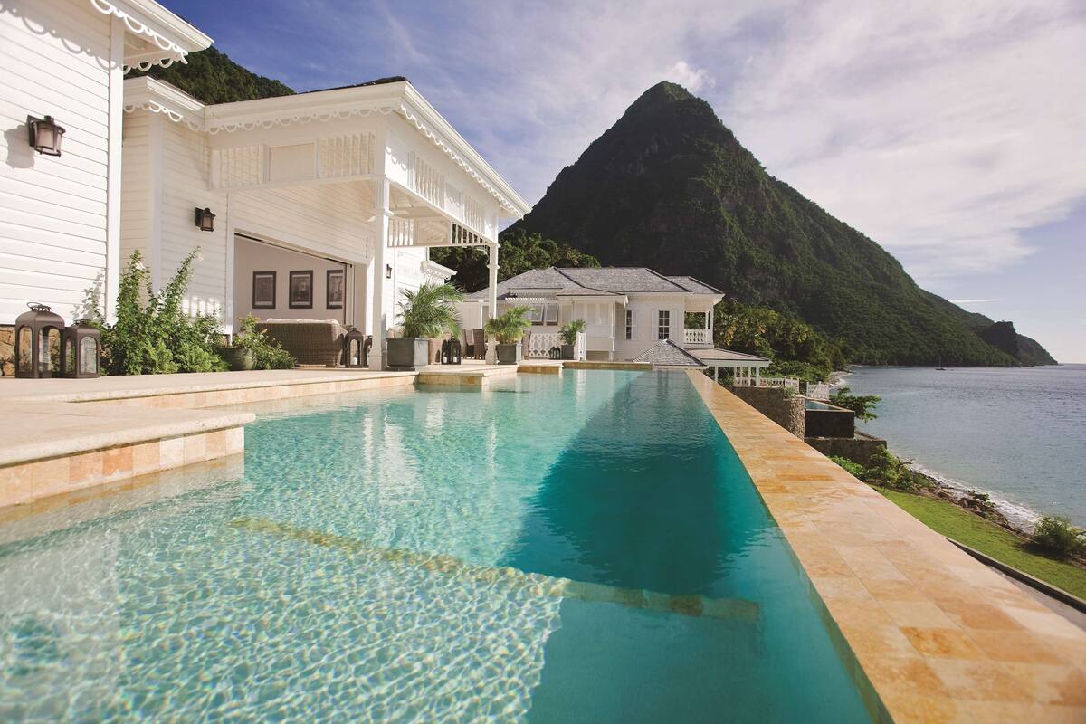 A swimming pool with a mountain backdrop, a white building with a balcony, and a view of the sea.