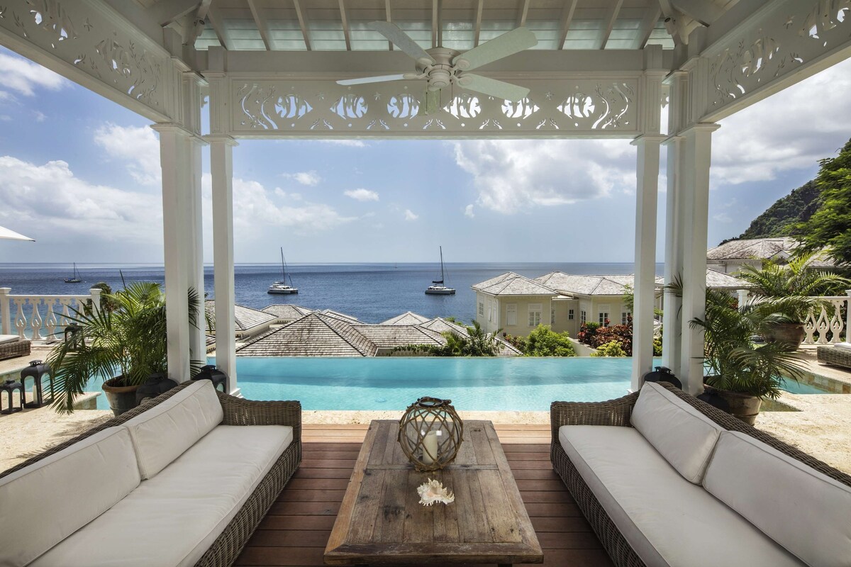 A covered outdoor seating area with a view of a pool and the sea.