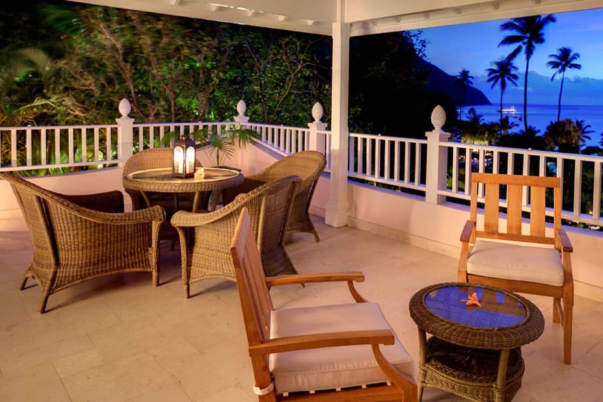A covered outdoor seating area with wicker furniture and a view of the ocean at dusk.