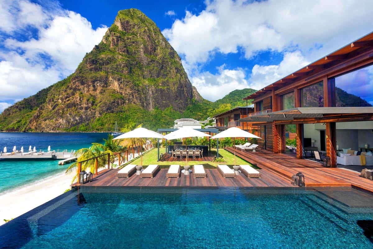 A resort with a pool, lounge chairs, umbrellas, and a mountain view.