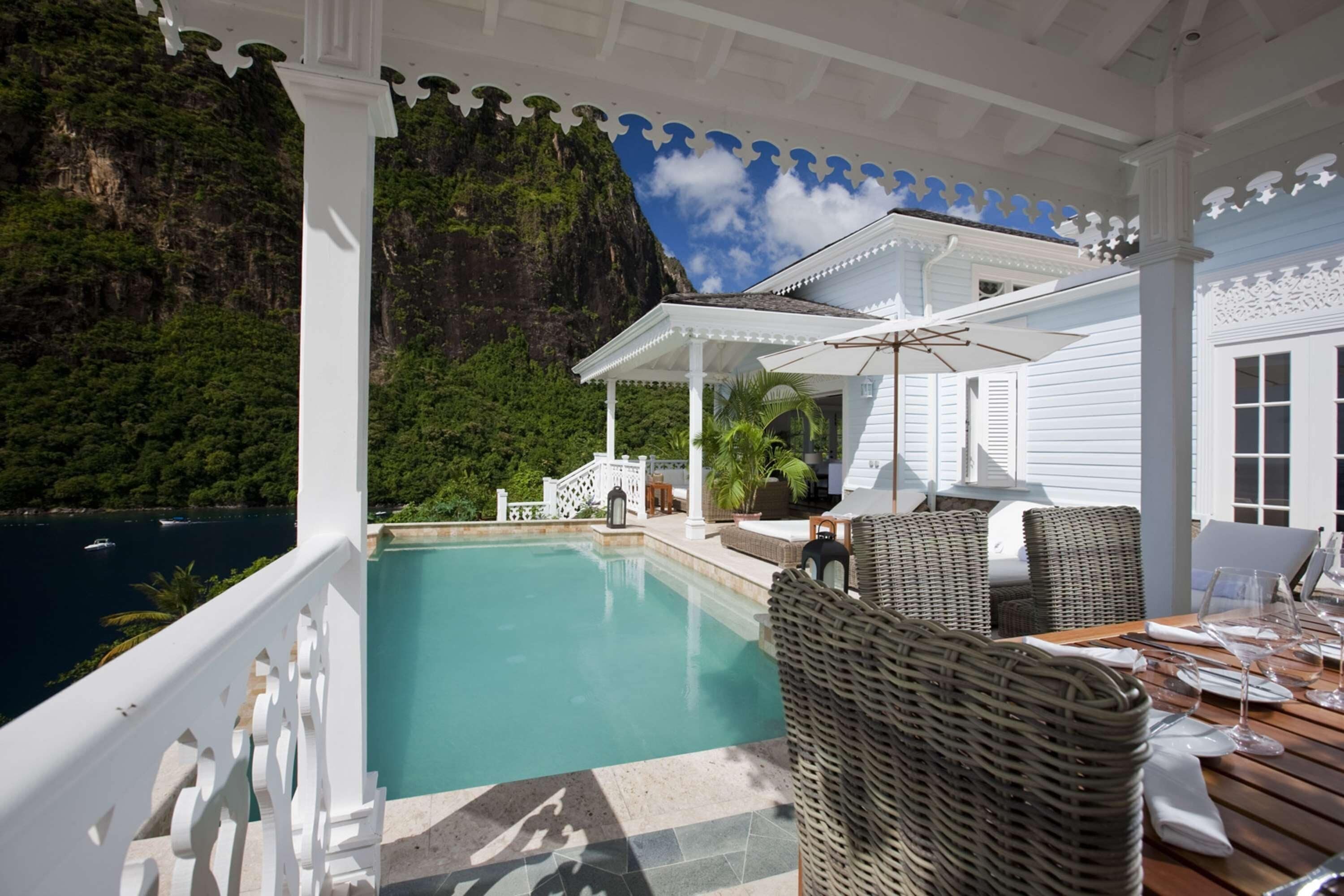 Un espace extérieur abrité, doté d'une piscine, de meubles en osier et offrant une vue sur une côte montagneuse.