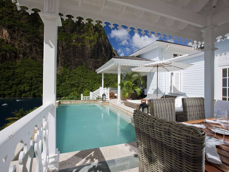 Un espace extérieur abrité, doté d'une piscine, de meubles en osier et offrant une vue sur une côte montagneuse.