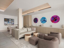 Una sala de estar moderna con un sofá, otomanas y una mesa de centro. Hay dos cuadros abstractos en la pared y un adorno sobre la mesa de centro.