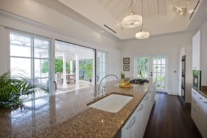 A modern kitchen with a granite countertop, stainless steel appliances, and large windows offering a view of the outdoors.