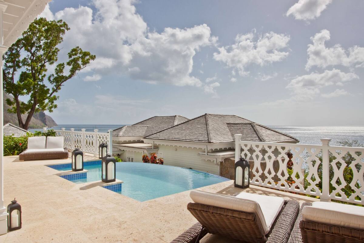 A poolside area with lounge chairs, a pool, and a view of the ocean.