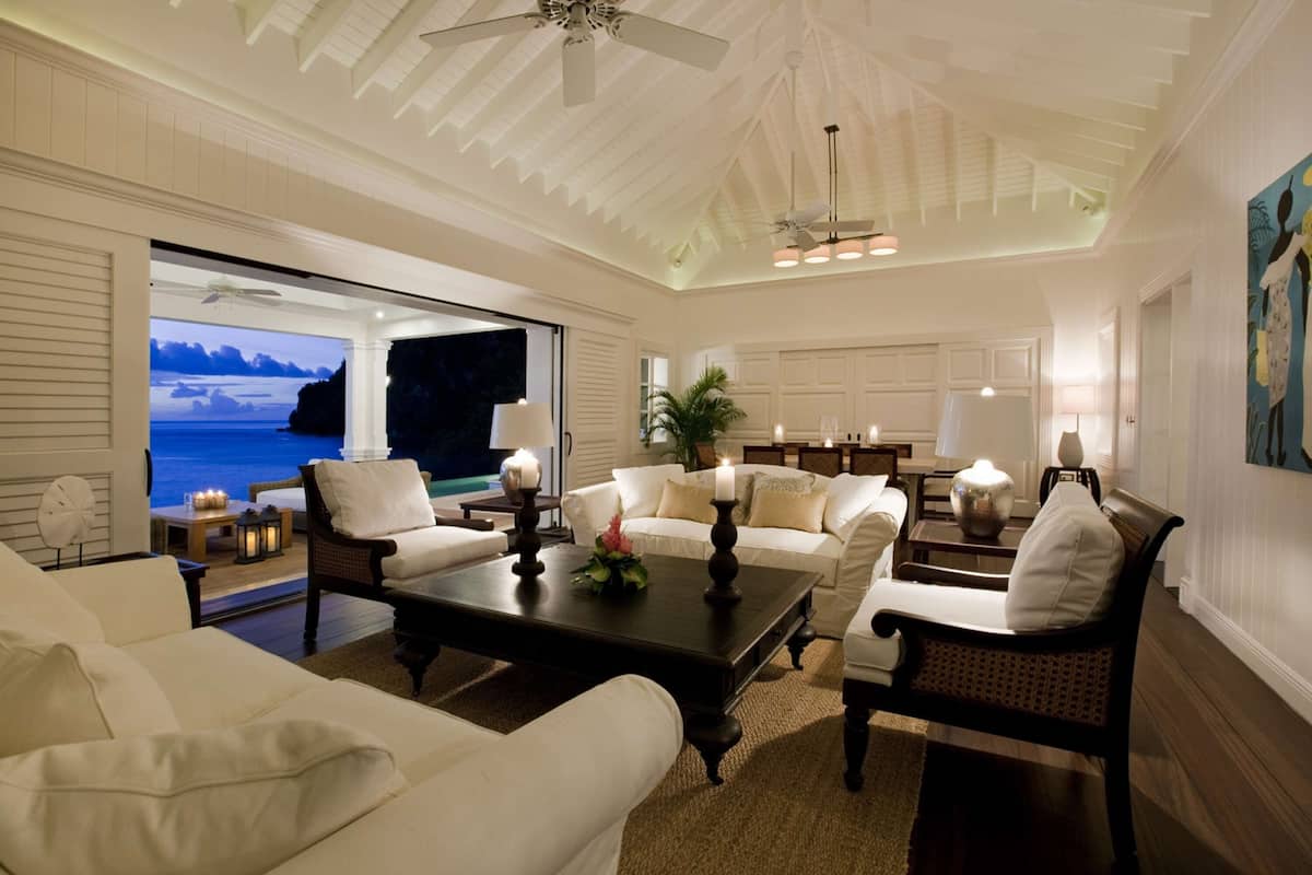 A spacious living room with a large window overlooking a scenic view, furnished with white sofas, a dark wooden coffee table, and elegant lighting fixtures.