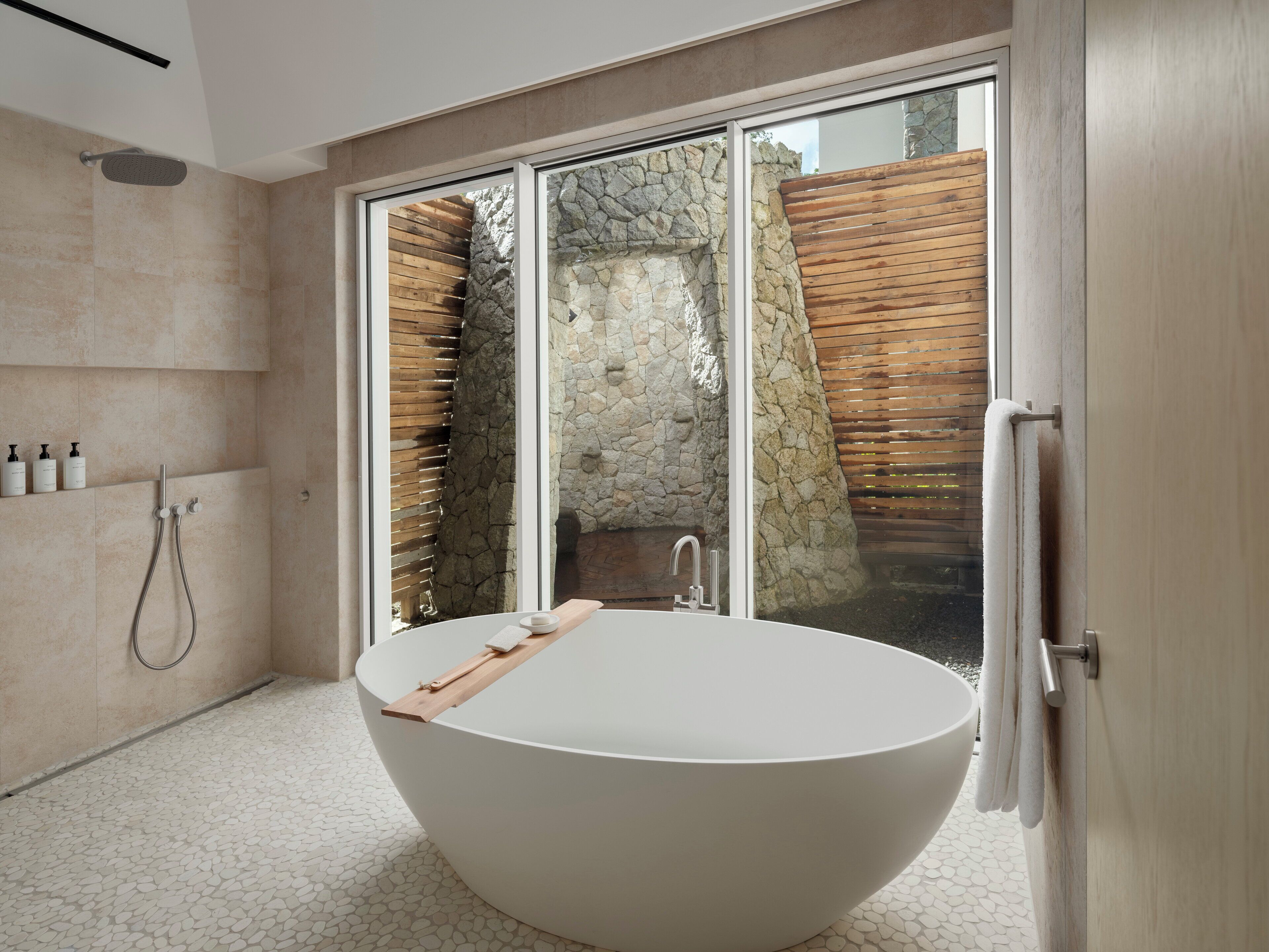 Ein modernes Badezimmer mit einer freistehenden Badewanne, einer Dusche und einer sichtbaren Steinwand hinter einer Glastür.
