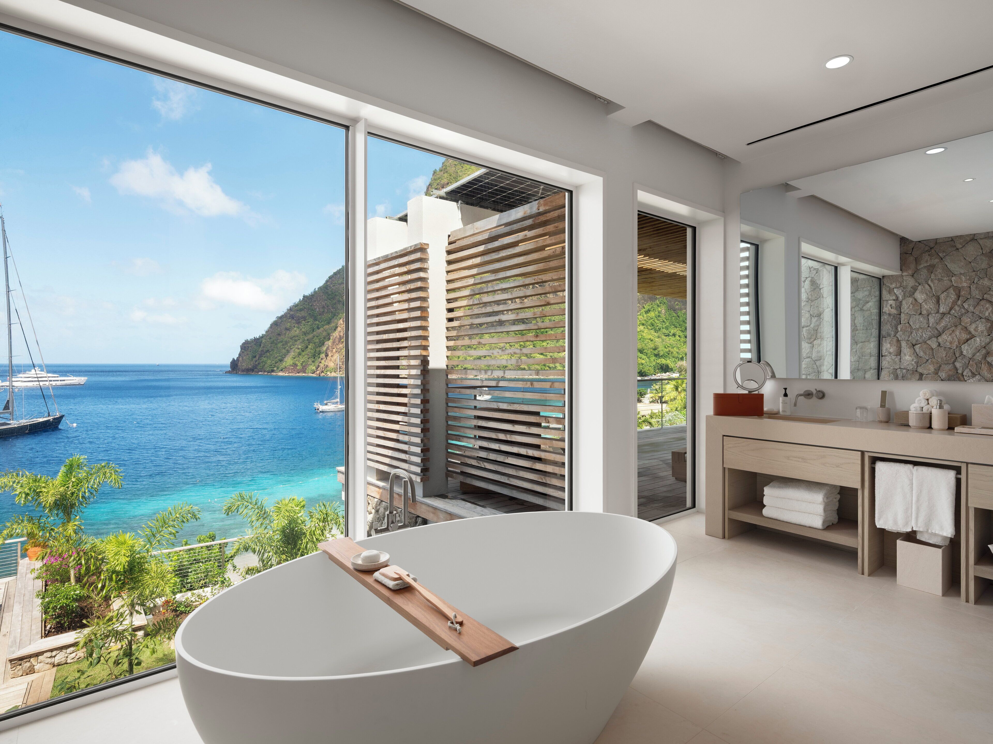 A modern bathroom with a large bathtub, a vanity with a mirror, and a view of the ocean.