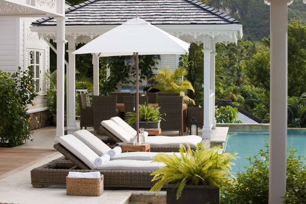 A poolside lounge area with wicker furniture, a white umbrella, and a view of a swimming pool.
