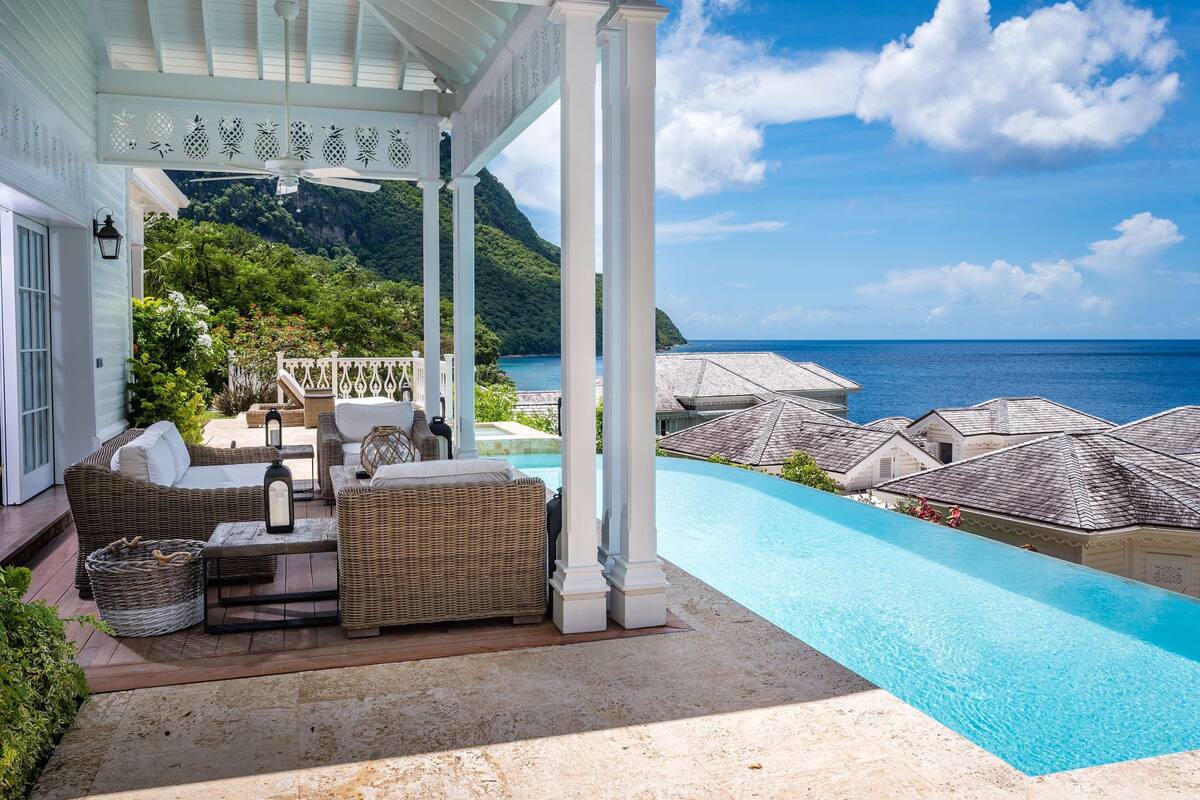 A covered outdoor area with wicker furniture, a pool, and a view of the ocean and mountains.