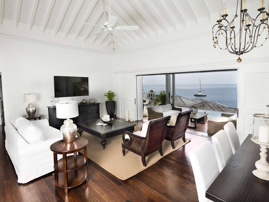 A spacious living room with a white sofa, dark wooden coffee table, and a view of the ocean through large windows.