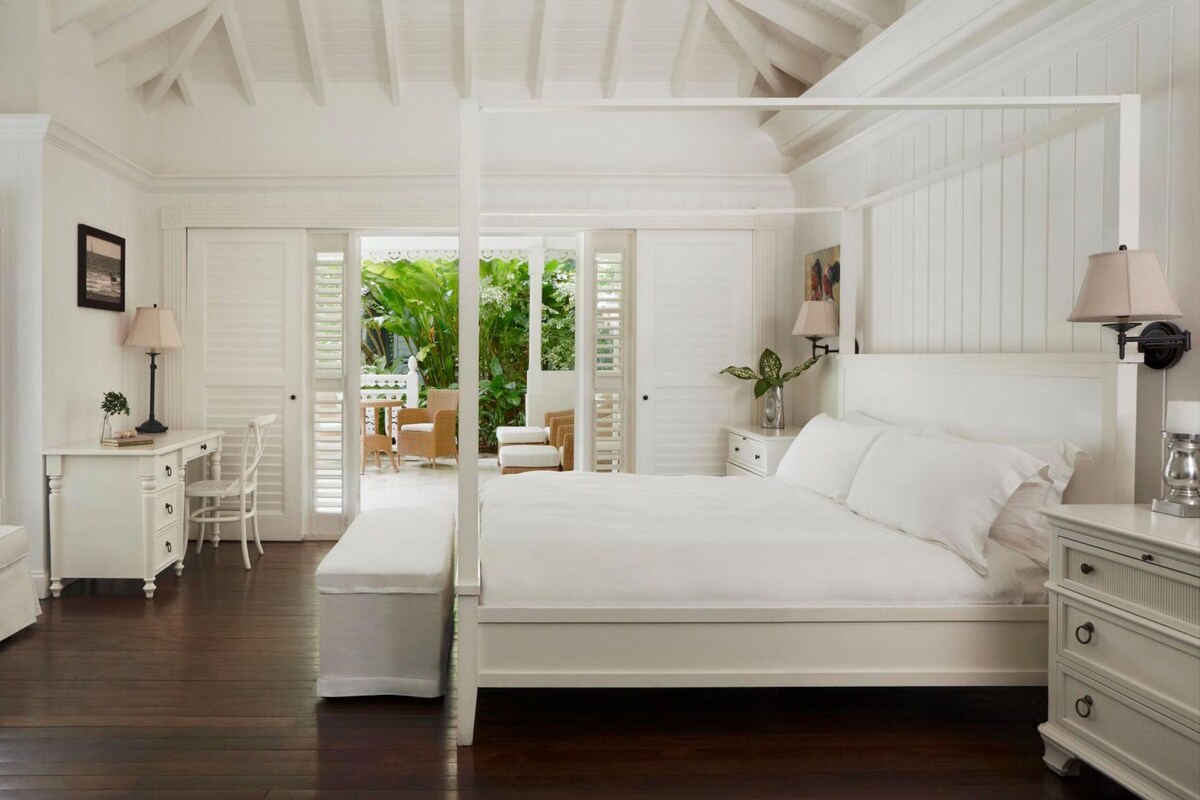 A spacious bedroom with a large bed, a desk, and a seating area with a view of the garden.