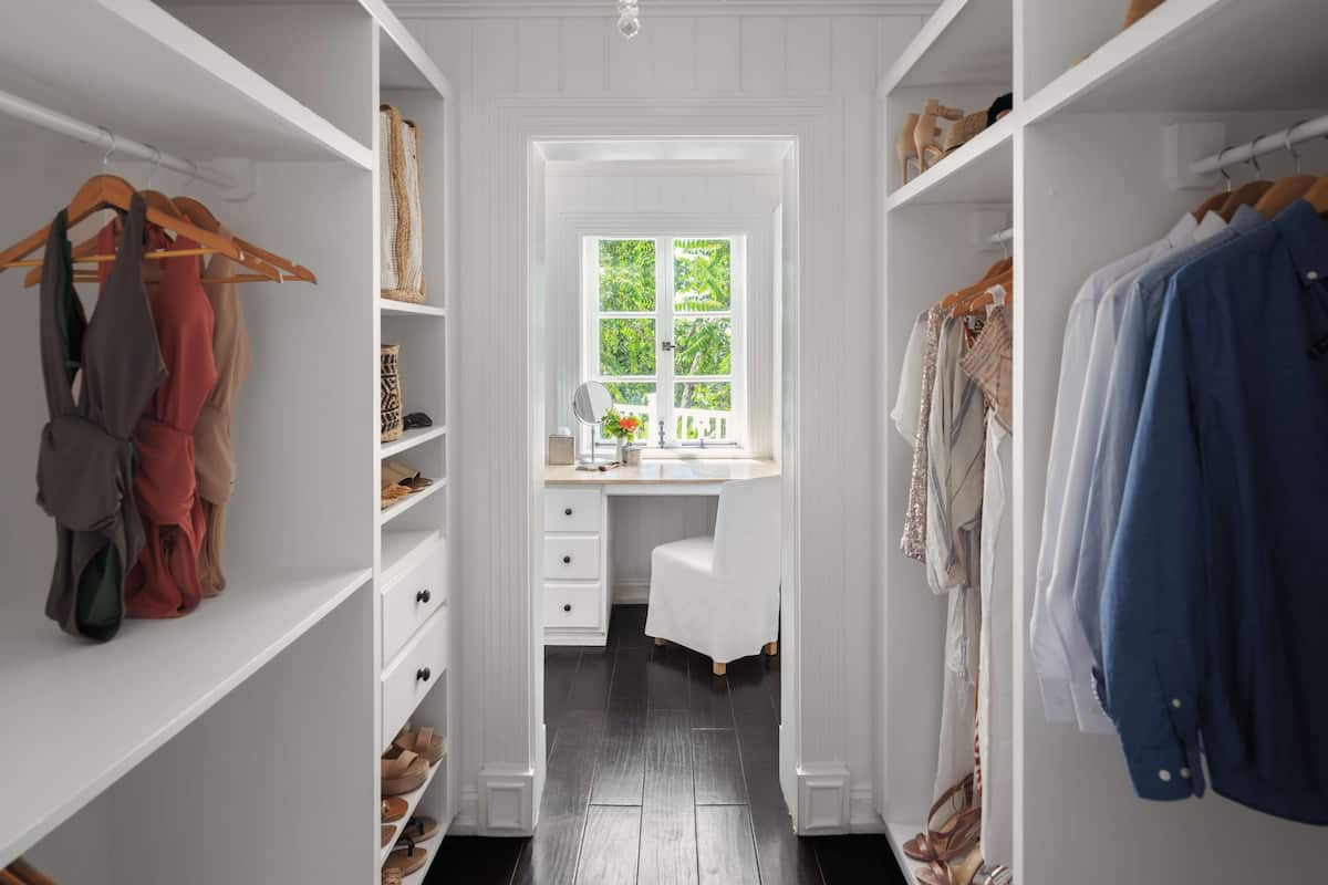 A walk-in closet with white shelving, a desk with a window, and a chandelier.