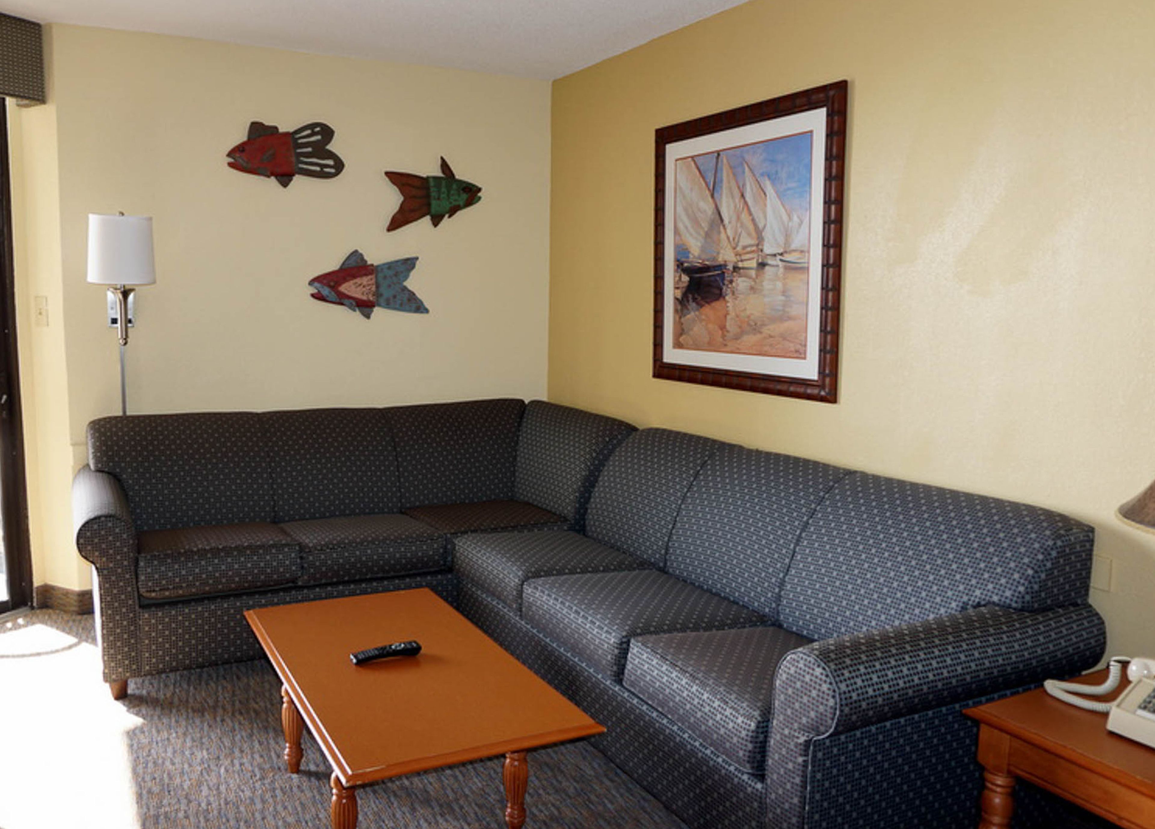 A living room with a sectional sofa, a coffee table, a lamp, and wall decorations including fish and a sailboat painting.