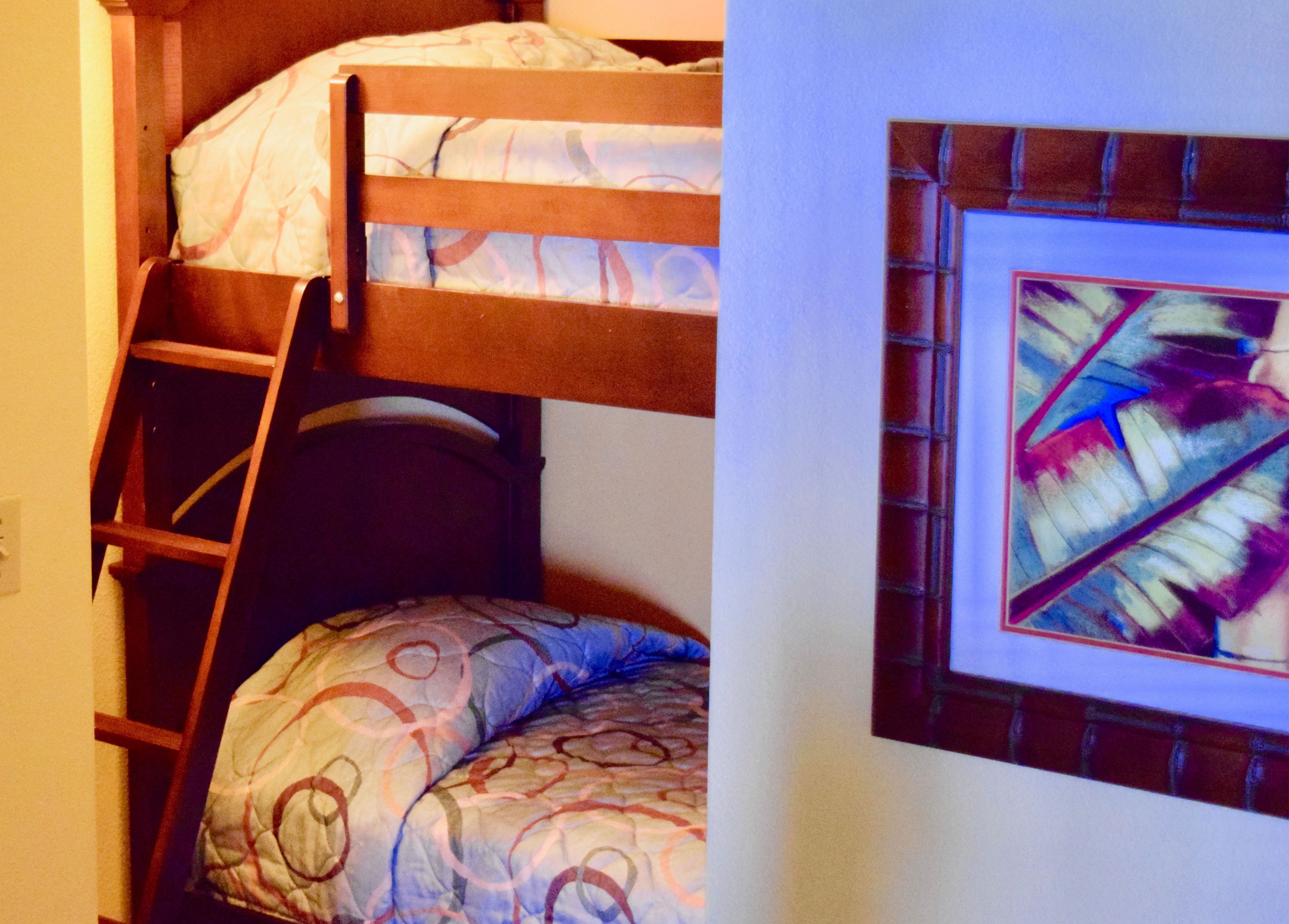 A bunk bed with a ladder, a pillow, and a framed abstract painting on the wall.