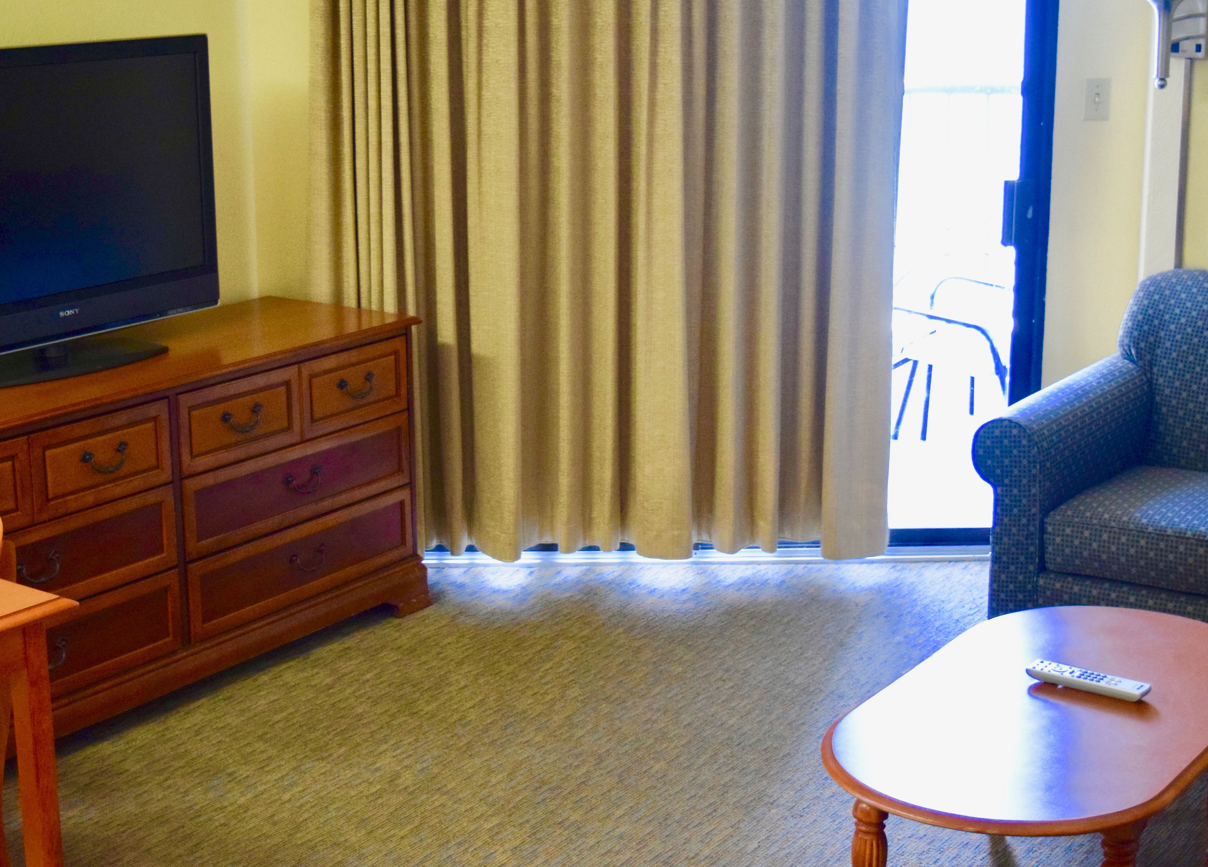 Een hotelkamer met een houten dressoir, een televisie, een bank en een afstandsbediening op een bijzettafeltje.