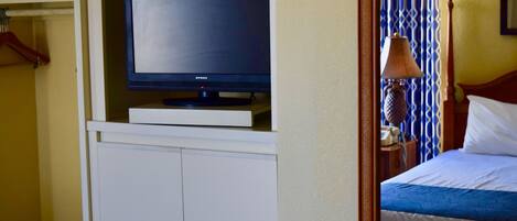 A hotel room with a television on a white cabinet, a bed with a blue bedspread, and a patterned curtain.