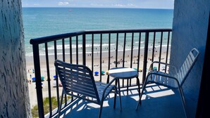 A balcony with two chairs and a small table, overlooking a beach with people and a parasail in the distance. - Schooner II Beach and Racquet Club (Myrtle Beach)