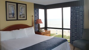 A hotel room with a large bed, a nightstand, a lamp, and a view of the beach. - Schooner II Beach and Racquet Club (Myrtle Beach)