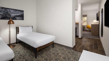 A modern hotel room with a single bed, a desk, a chair, a lamp, and a painting on the wall.