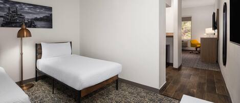 Ein modernes Hotelzimmer mit einem Einzelbett, einem Schreibtisch, einem Stuhl, einer Lampe und einem Bild an der Wand.