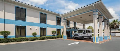 A hotel with a covered parking area, a van, and a clear sky.