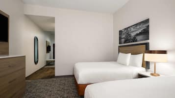 Een hotelkamer met twee bedden, een houten dressoir, een spiegel, een inlijsting foto aan de muur en een lamp op het nachtkastje.