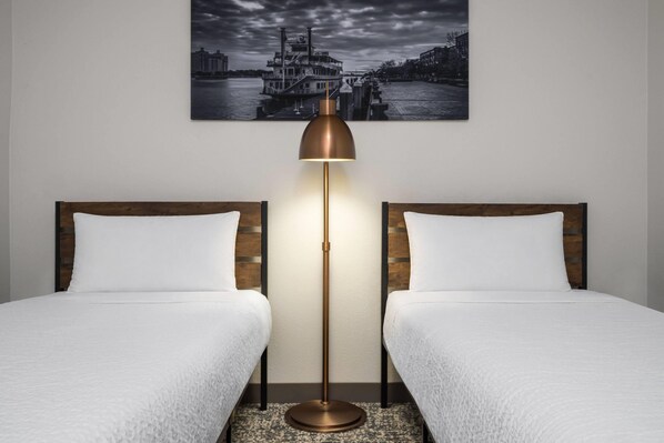 A hotel room with two beds, a floor lamp, and a cityscape painting on the wall.