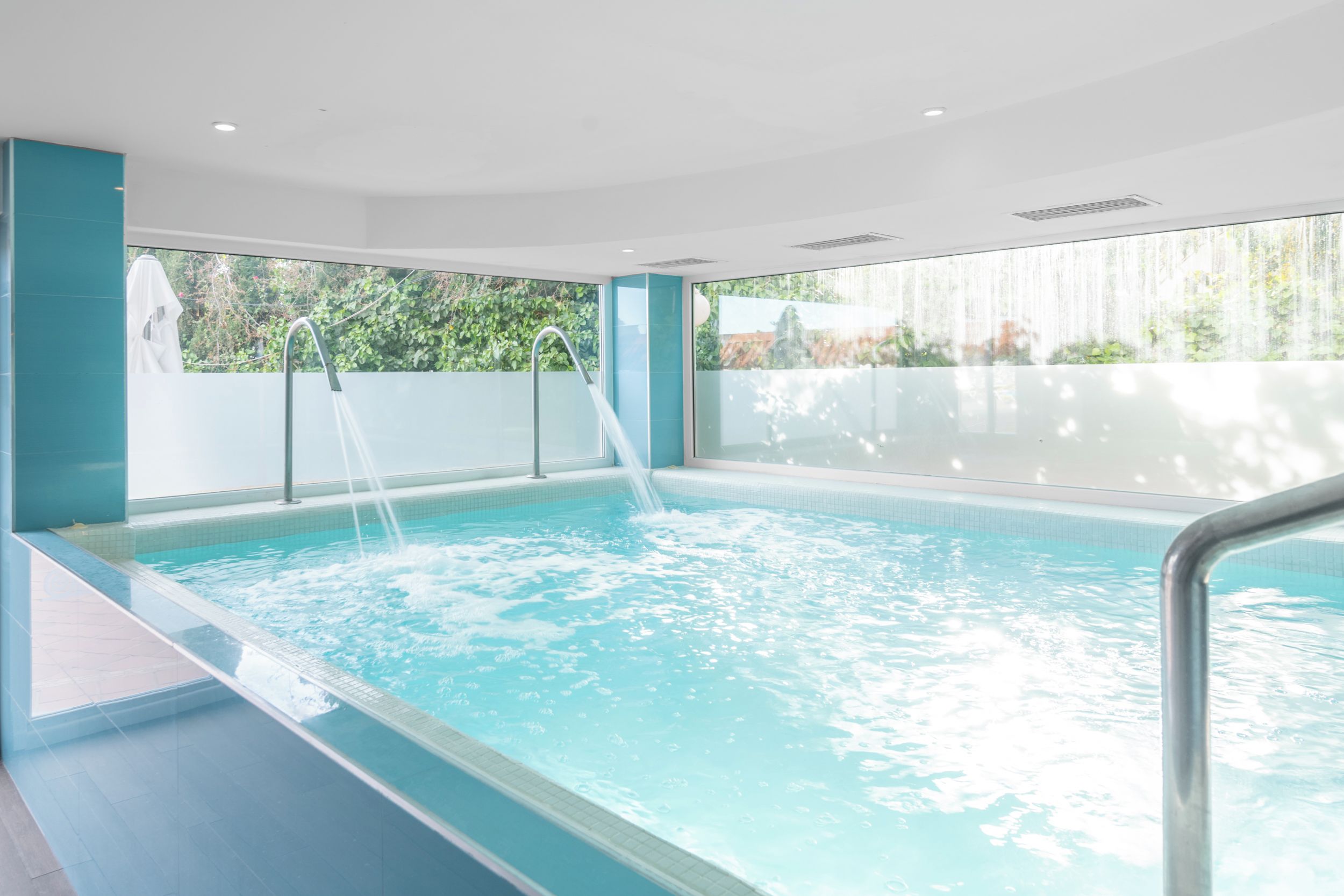 Una piscina con agua cristalina, una barrera de vidrio y vistas a la vegetación circundante.