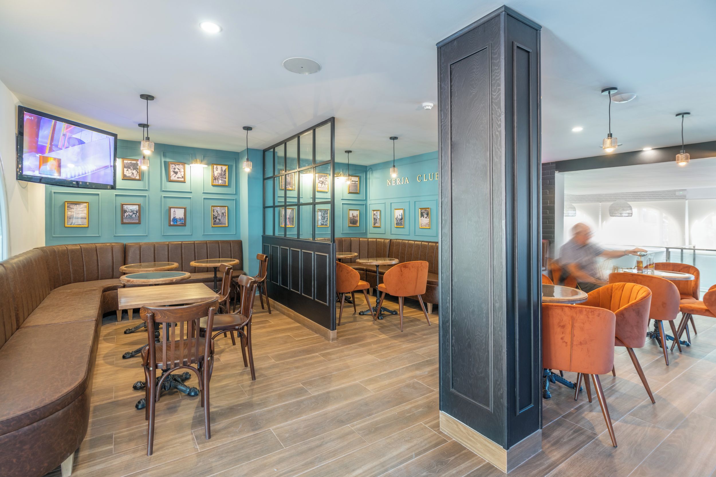 A modern restaurant with a teal color scheme, wooden flooring, and a variety of seating options including booths and tables.
