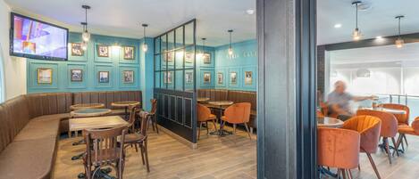 A modern restaurant with a teal color scheme, wooden flooring, and a variety of seating options including booths and tables.