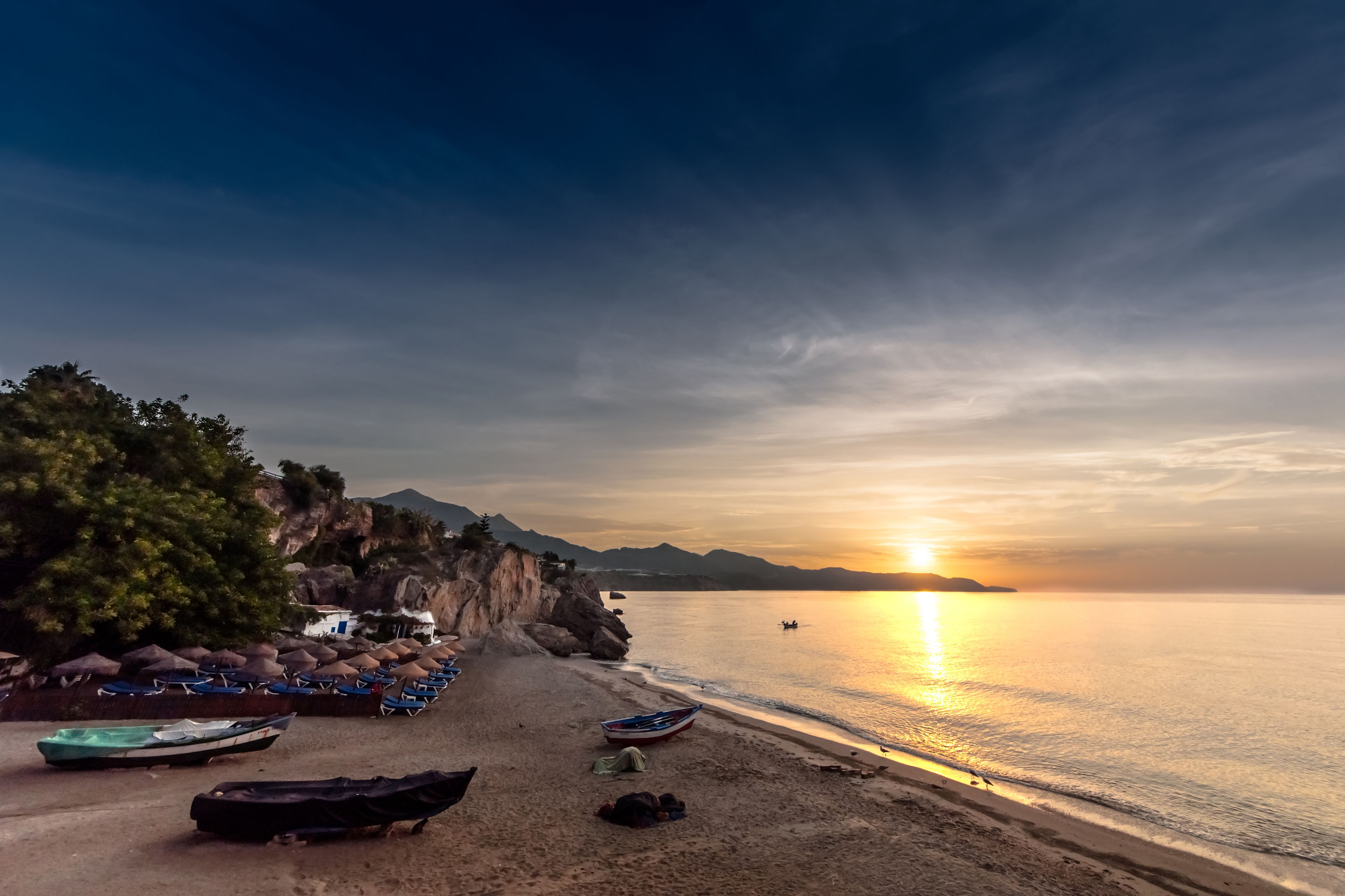 A beach with boats, a tent, and a rocky cliff.