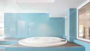 Een moderne badkamer met een centraal gelegen whirlpool, blauwe betegelde wanden en een groot raam.
