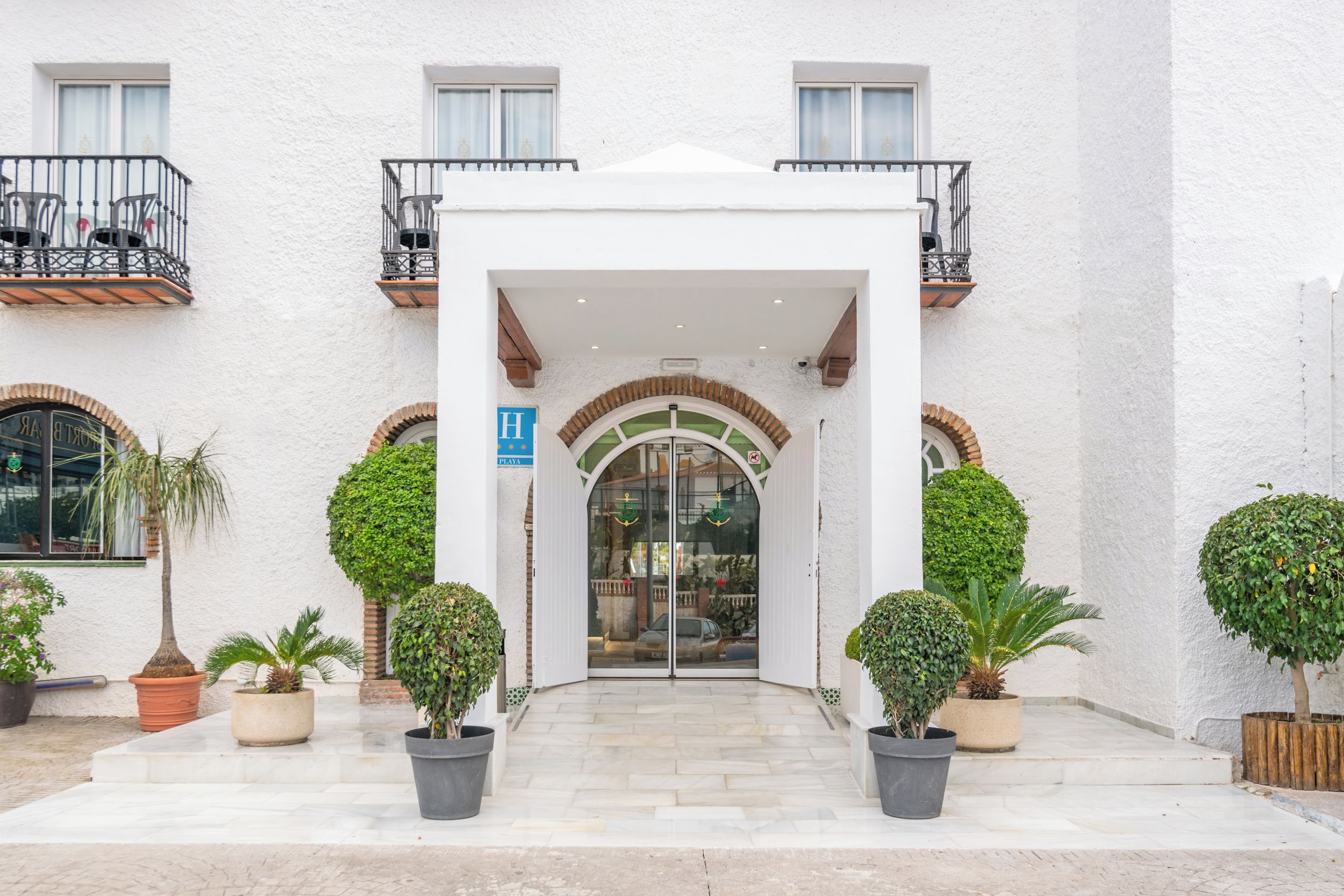 A hotel entrance with a white facade, a glass door, and a balcony with metal railings.