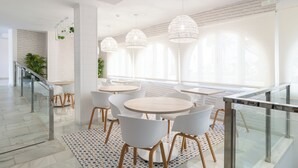 A modern dining area with round tables and white chairs, large windows with natural light, and a staircase with glass railings. - Nerja Club by Dorobe (Nerja)