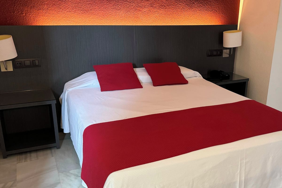 A hotel room with a large bed, two nightstands, and a wall-mounted lamp.