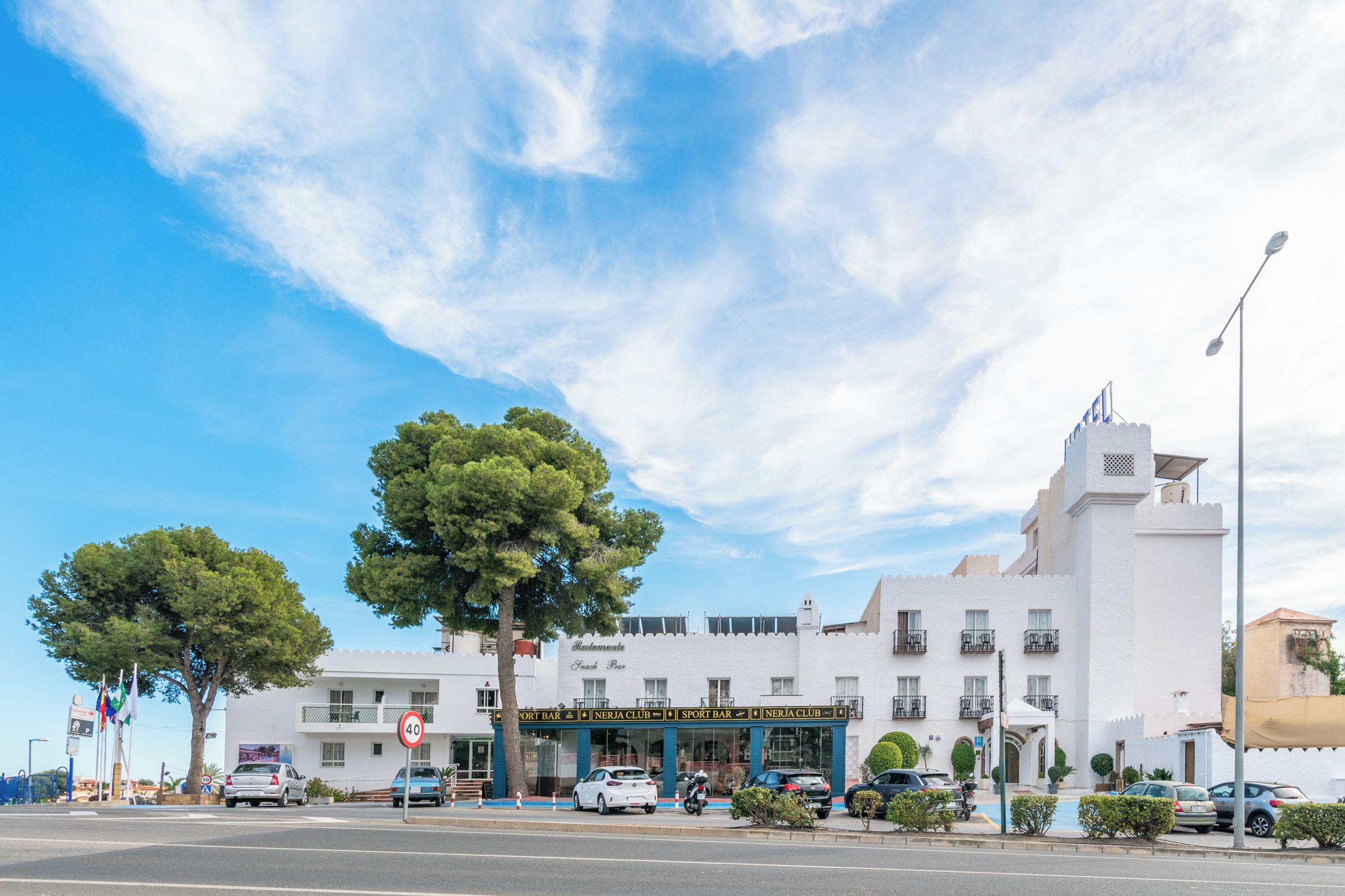 Un bâtiment blanc à étages, une enseigne indiquant un bar sportif et un panneau de signalisation indiquant une limite de vitesse de 40.