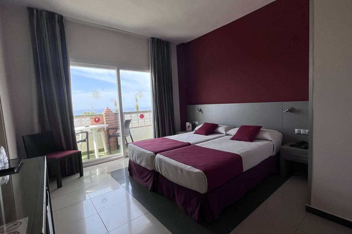 Una habitación de hotel moderna con una cama grande, un escritorio y un balcón con vistas.