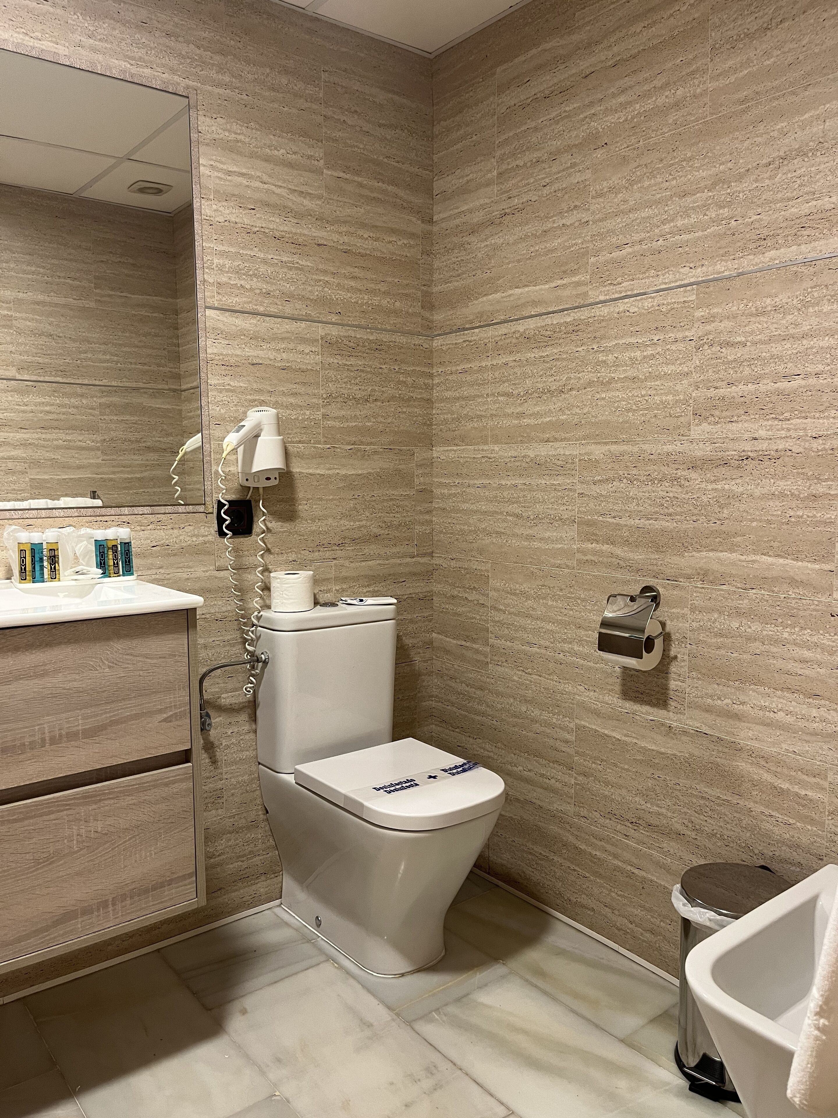 Une salle de bain équipée de toilettes, d’un lavabo, d’un miroir et d’une poubelle.