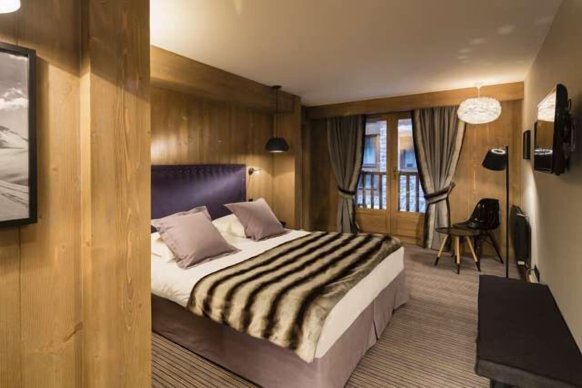 Ein Schlafzimmer mit einem großen Bett, Holzwänden, einem Fenster mit Vorhängen und einem Schreibtisch mit Stuhl.