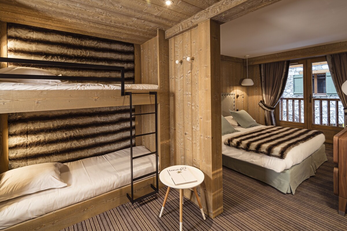 Ein Zimmer mit Etagenbetten, einem Einzelbett, einem kleinen Tisch und einem Fenster mit Vorhängen.